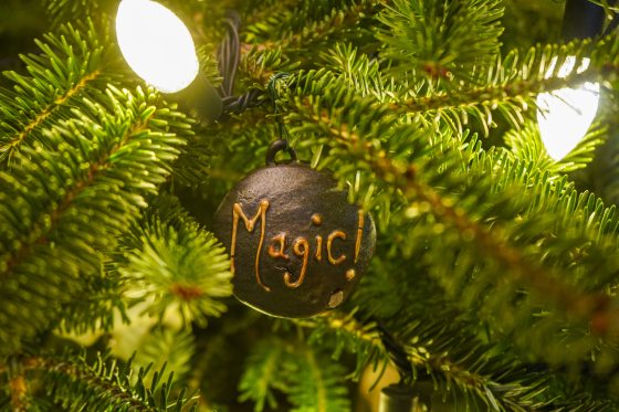A round ornament hanging on a Christmas tree that reads "Magic!"